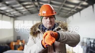 戴着安全帽、穿着工作服的人正站在机库的中间，看着他的手表